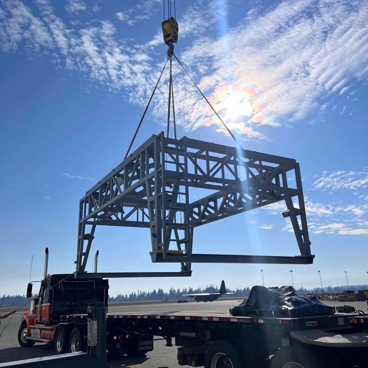 Structural steel frame being lifted by crane onto a flatbed trailer at an industrial yard